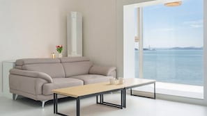 Una sala de estar moderna con sofá, una mesa de centro y vista a un cuerpo de agua a través de un ventanal grande.