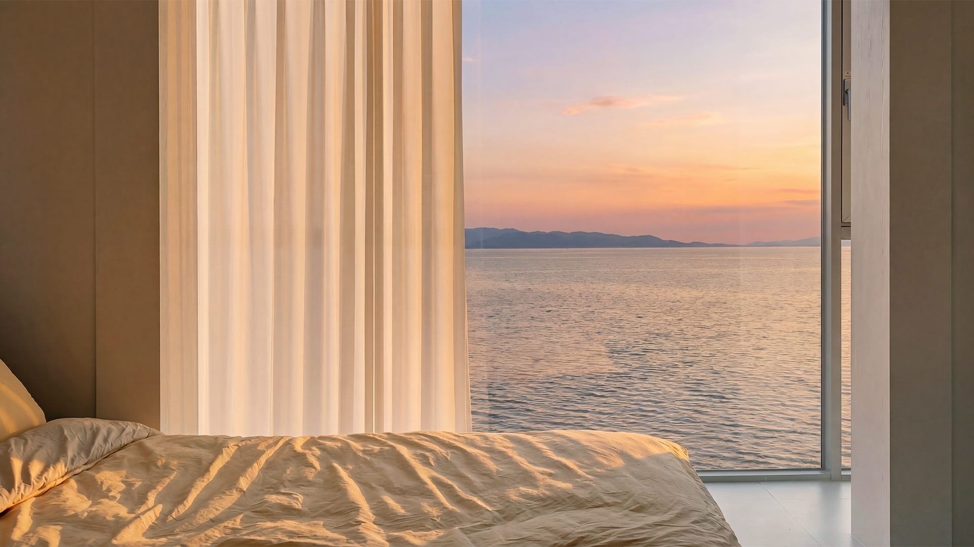 A bedroom with a large window overlooking a body of water at sunset.