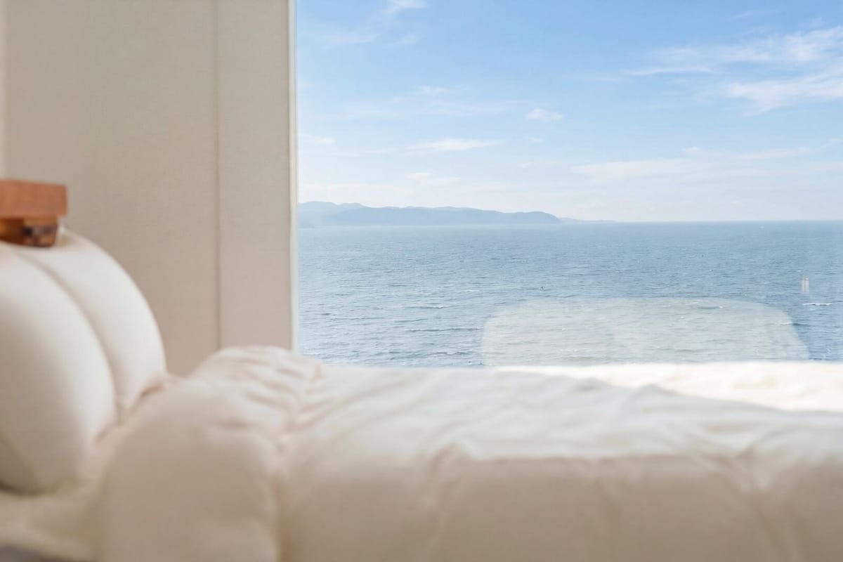 A bed with a headboard, a window with a view of the sea, and a wooden headboard.