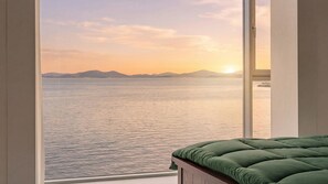 A room with a large window overlooking a body of water and distant mountains during sunset. - Daebudo Sunbell Ocean View Pension (Ansan)
