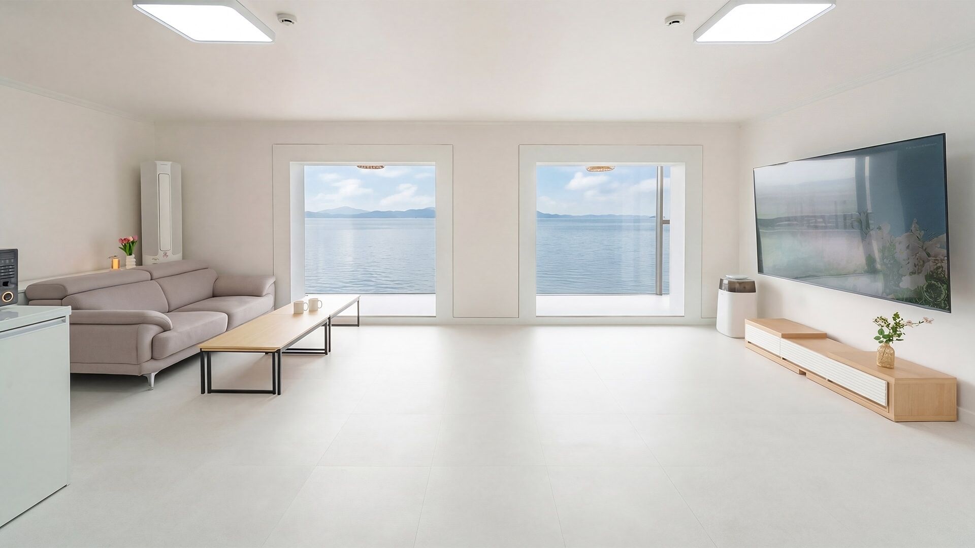 Una sala de estar moderna con sofá, mesa de centro, televisor y grandes ventanales con vista a un cuerpo de agua.