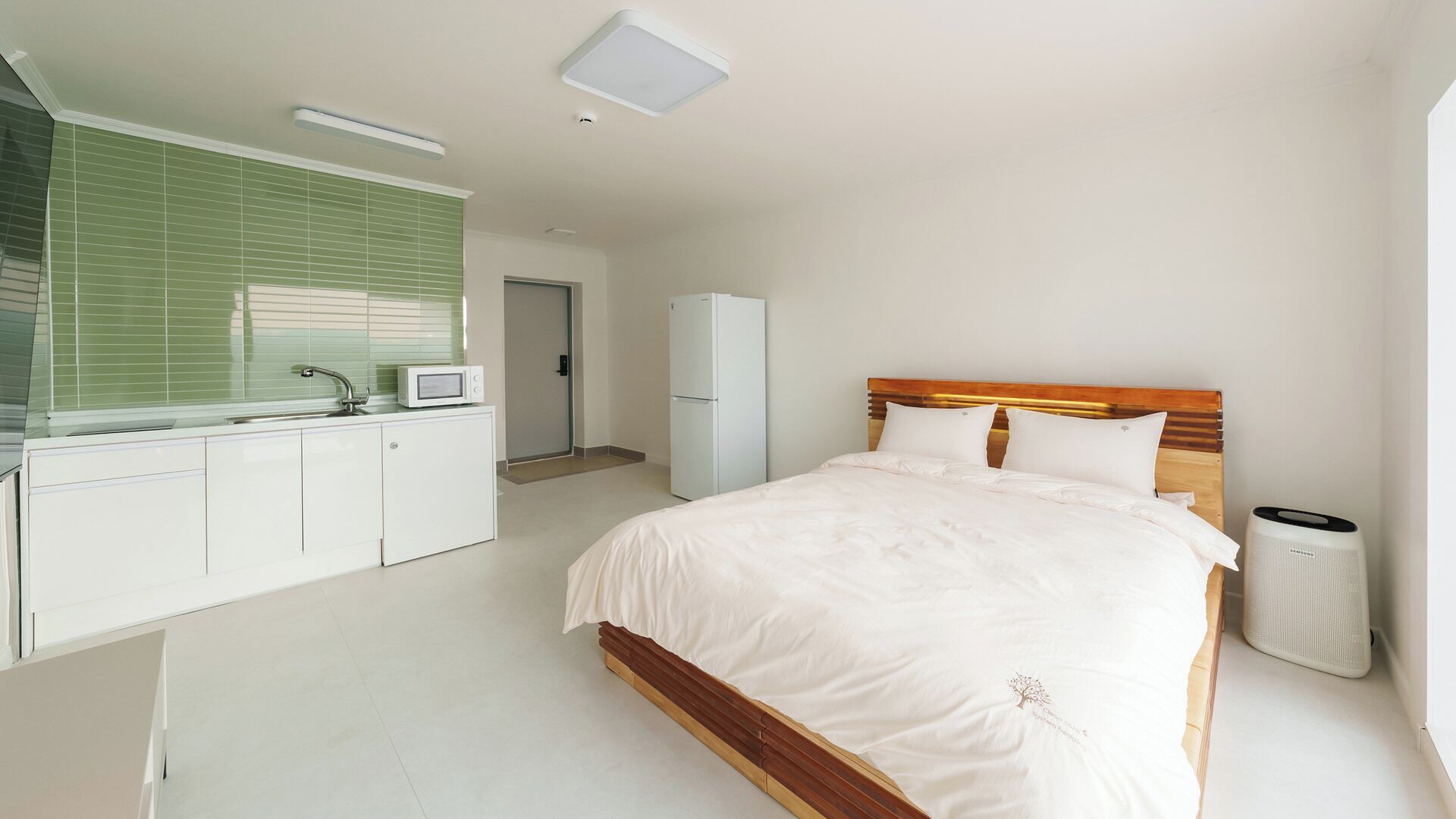 A bedroom with a bed, a microwave, a refrigerator, and a trash bin.