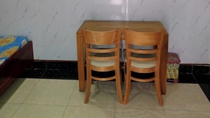 A dining area with a marble-patterned wall, a wooden table with two chairs, and a small trash bin. - Nha nghi Nguyen Bao  - Tran De Con Dao (Can Tho)