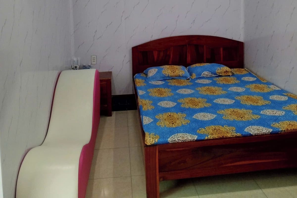 A bedroom with a bed, a bedside table, a chair, and an air conditioning unit.