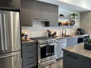 A modern kitchen with stainless steel appliances, grey cabinetry, and a built-in oven. - Moonlight Ascent | Pool, Hot Tub, Gym | Parking (Canmore)