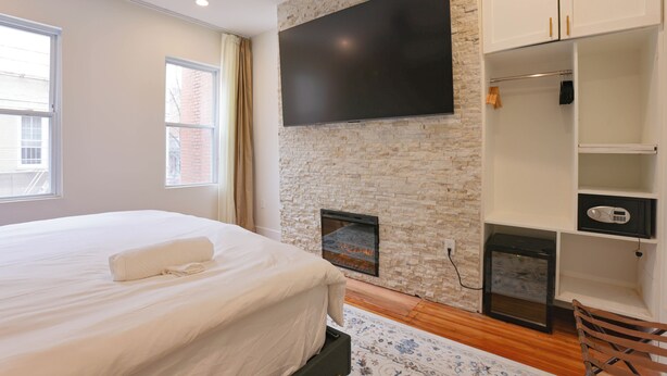 Un dormitorio con una cama grande, un televisor de pantalla plana montado en una pared de piedra, una chimenea y un armario.