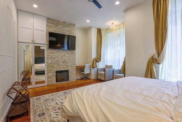 A bedroom with a bed, a fireplace, a TV, and a seating area with chairs.