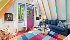 Um interior acolhedor e colorido com um sofá azul, um chão vibrante em xadrez e uma grande janela com porta roxa.