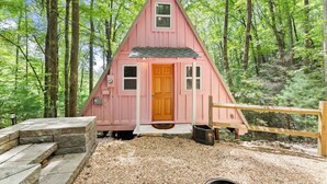 Uma cabana rosa com porta e janelas de madeira, e uma entrada com calçada de cascalho.