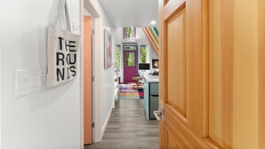 Um corredor com um porta-roupas, um interruptor de luz na parede e um tapete colorido que leva a um quarto com uma porta roxa.