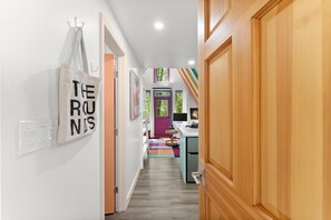 A hallway with a coat rack, a wall-mounted light switch, and a colorful rug leading to a room with a purple door. - Color Me Cozy A-Frame - Stylish North Georgia Cabin Near Helen (Cleveland)