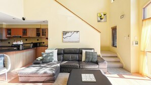 A living room with a sectional sofa, a coffee table, a staircase, and a kitchen area. - Coastal Holiday Home - Bradford 10 (Labrador)