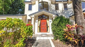 A two-story house with a red door, a small porch, and a well-maintained garden with various plants. - Coastal Holiday Home - Bradford 10 (Labrador)