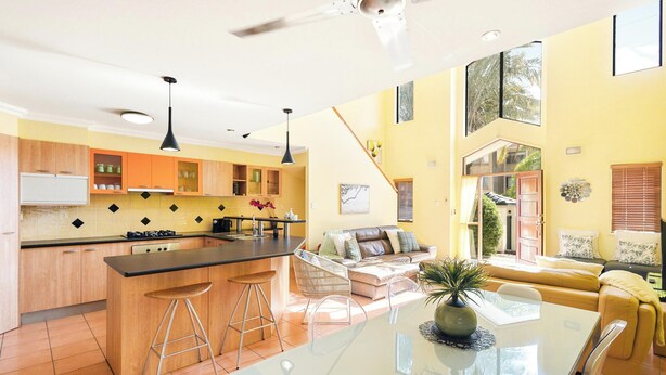 A modern kitchen with a central island, bar stools, a dining table with chairs, a sofa, and a staircase leading to an upper level. - Coastal Holiday Home - Bradford 10 (Labrador)