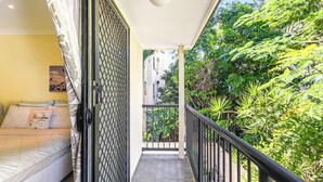 A balcony with a view of lush greenery, a bed with patterned bedding, and a ceiling light fixture. - Coastal Holiday Home - Bradford 10 (Labrador)