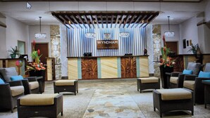 A reception area with a reception desk labeled 'WYNDHAM' and 'VACATION RESORT'. There are four wicker chairs with cushions arranged around the desk. The floor has a patterned tile design. - Spacious 2-BR/2-bath suite with full kitchen & living room, minutes from beach (Honolulu)