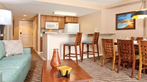 A compact living space with a kitchenette, a dining area with wooden chairs, a sofa, and a coffee table. - Spacious 2-BR/2-bath suite with full kitchen & living room, minutes from beach (Honolulu)