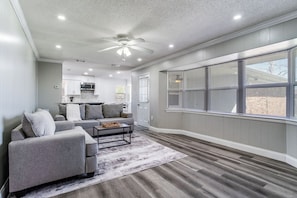 Ein geräumiges Wohnzimmer mit grauem Sofa, einem Couchtisch und einem Deckenventilator.