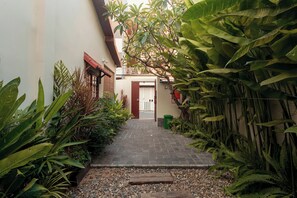 A narrow pathway leading to a building entrance, surrounded by lush greenery and a brick pathway. - An Nam Home (Da Nang)