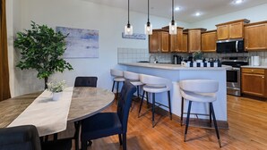 A modern kitchen with wooden cabinets, a central island with bar stools, pendant lighting, and a potted plant.