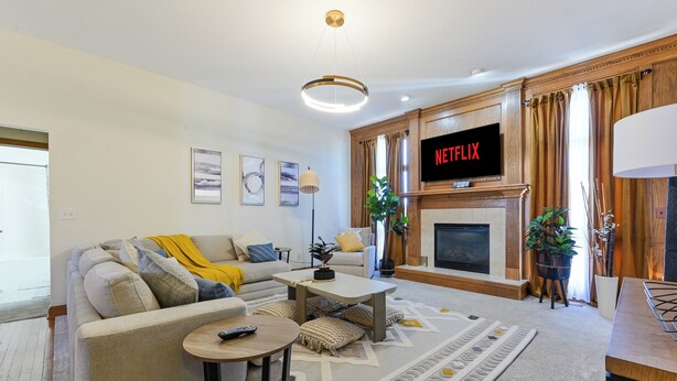 A living room with a sofa, coffee table, TV, fireplace, and decorative plants.