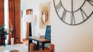 A room with a wooden door, a wall clock, a mirror, a lamp, and a sign with a quote.
