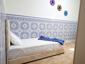 Un lit avec une tête de lit à motifs, un matelas blanc et un plaid bleu.
