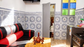 Een knus woongedeelte met een bank, een klein tafeltje met een vaas, een televisie en een kitchenette met een koelkast.