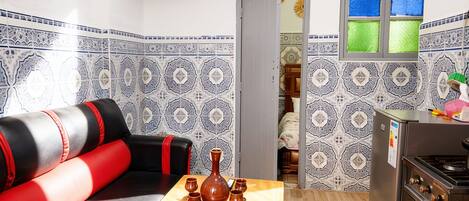 A compact living space with a sofa, a small table with a vase, a television, and a kitchen area with a refrigerator.