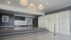 Un vestíbulo moderno con una mesa de recepción, tres lámparas colgantes, un perchero y una amplia pared blanca con taquillas.