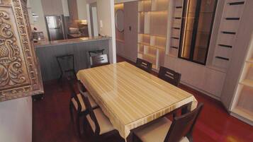 Un comedor con mantel a rayas, sillas de madera, una cocina al fondo y una pared decorativa con estanterías.