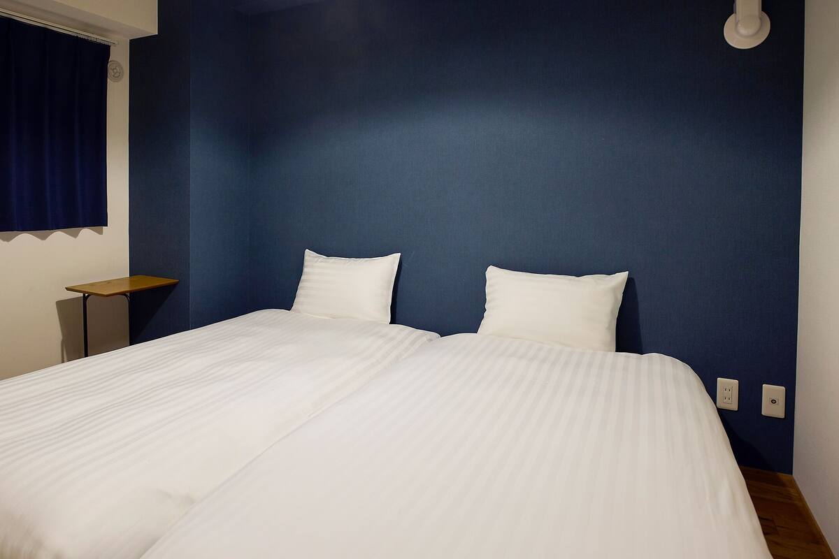 A double bed with white bedding in a room with blue walls and a wooden floor.