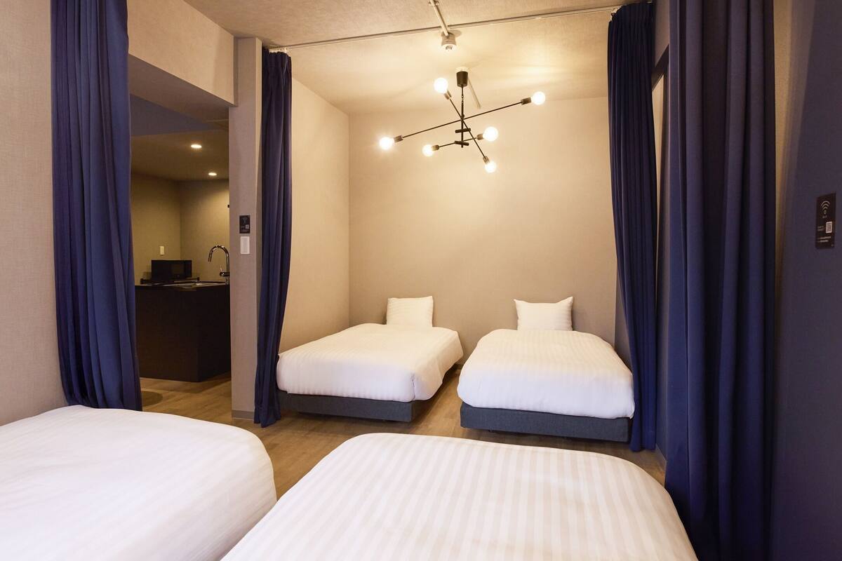 A hotel room with two beds, a desk, and a shower area.