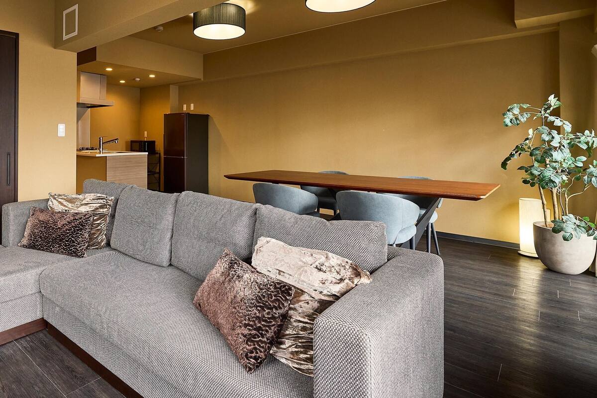 A modern living room with a sectional sofa, a dining table, and a kitchen area in the background.