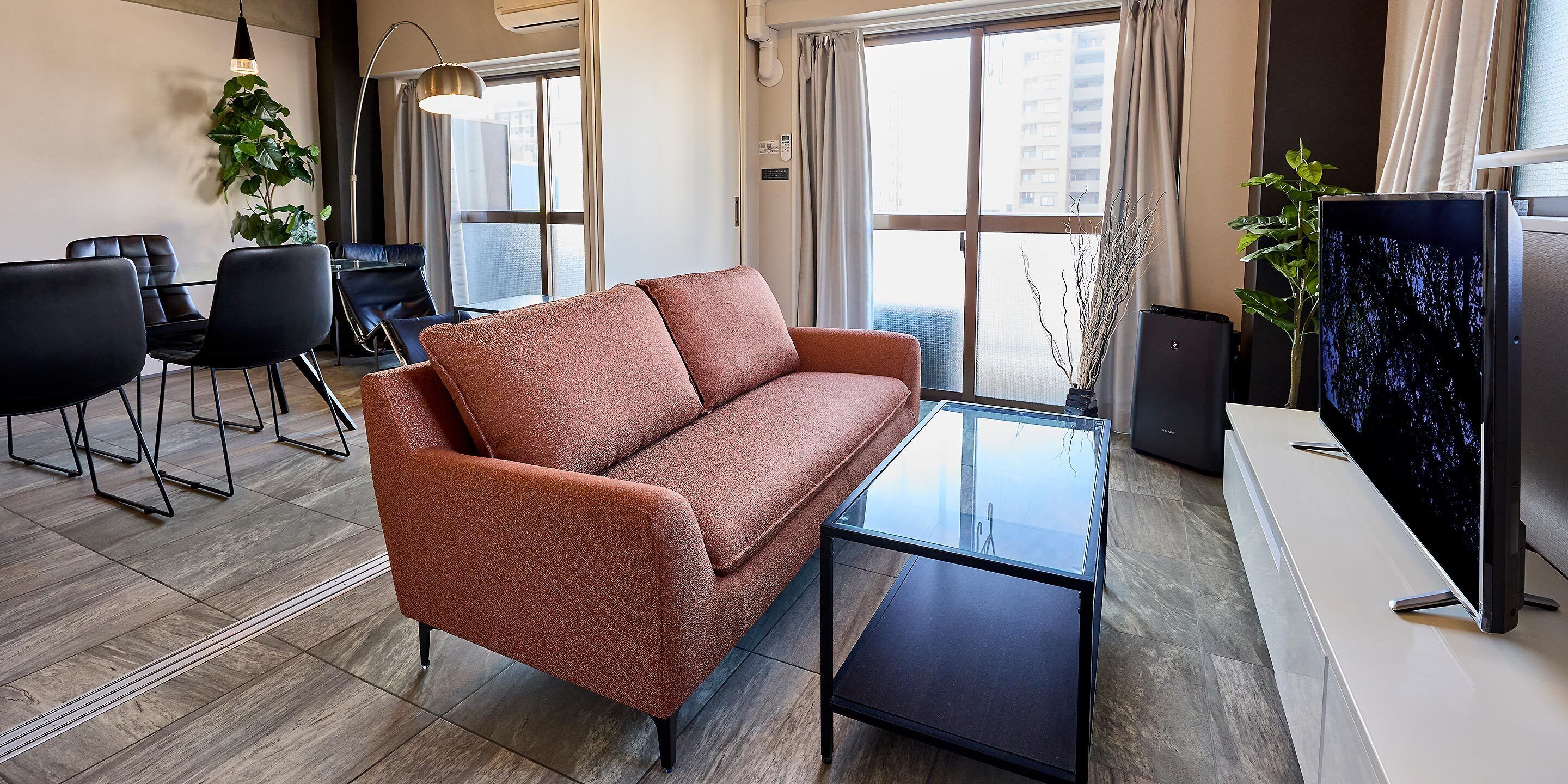 A modern living room with a sofa, a glass coffee table, a TV, and a dining area with chairs and a table.