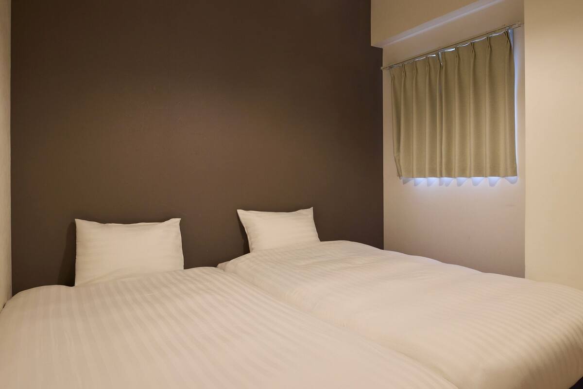 A double bed with two pillows, a window with curtains, and a brown wall.