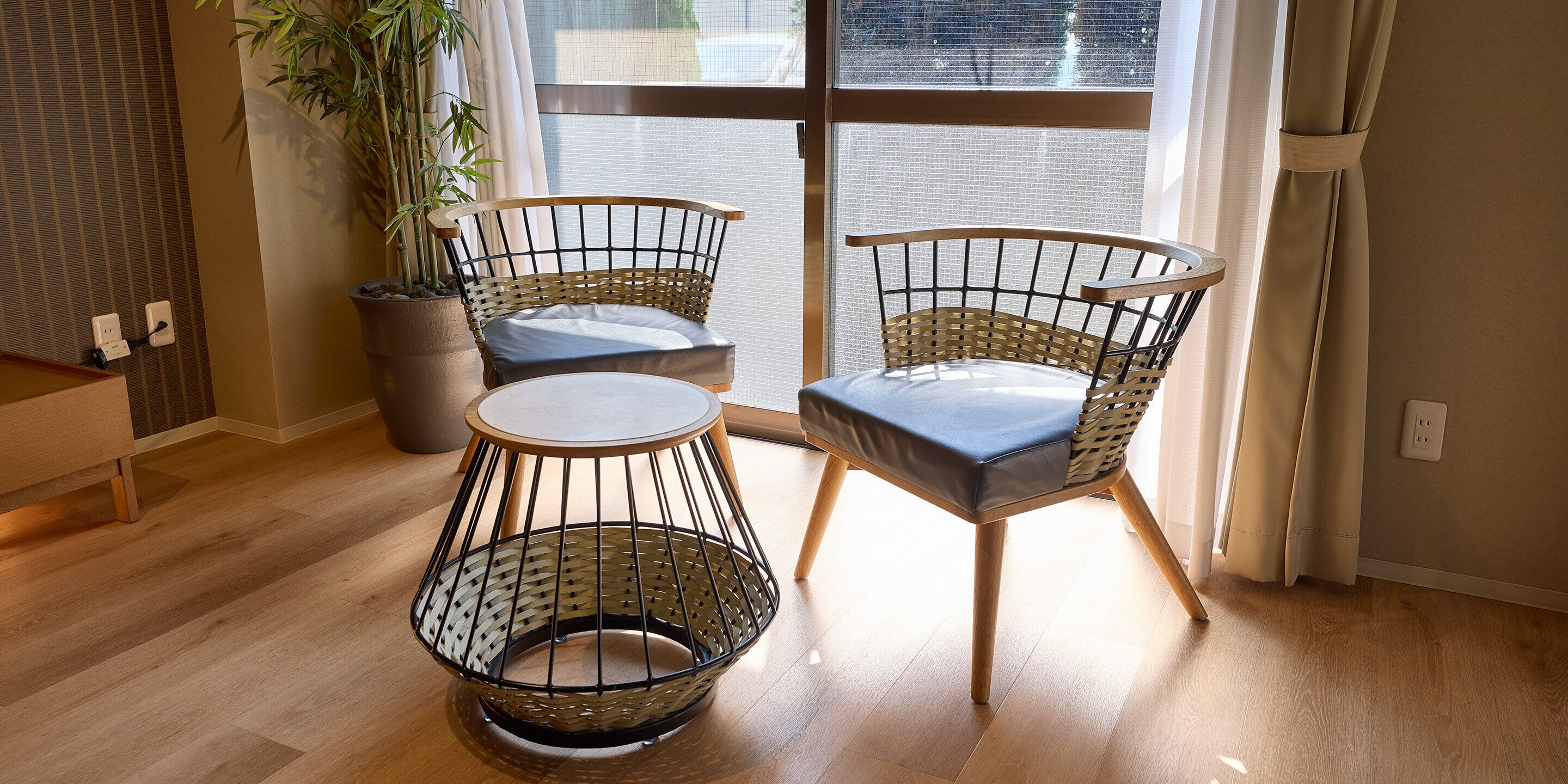 A room with two wicker chairs, a small round table, and a potted plant.