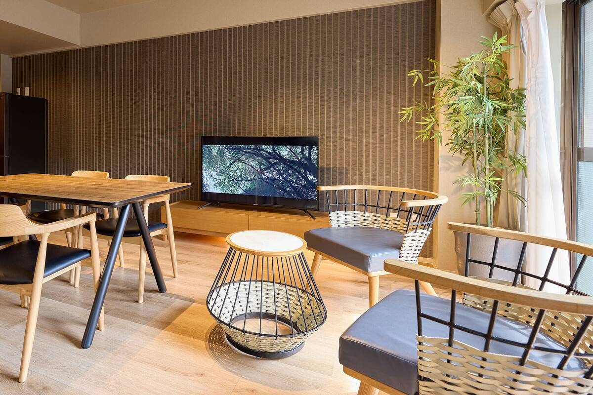 A modern living room with a dining table, chairs, a television, and a large plant.