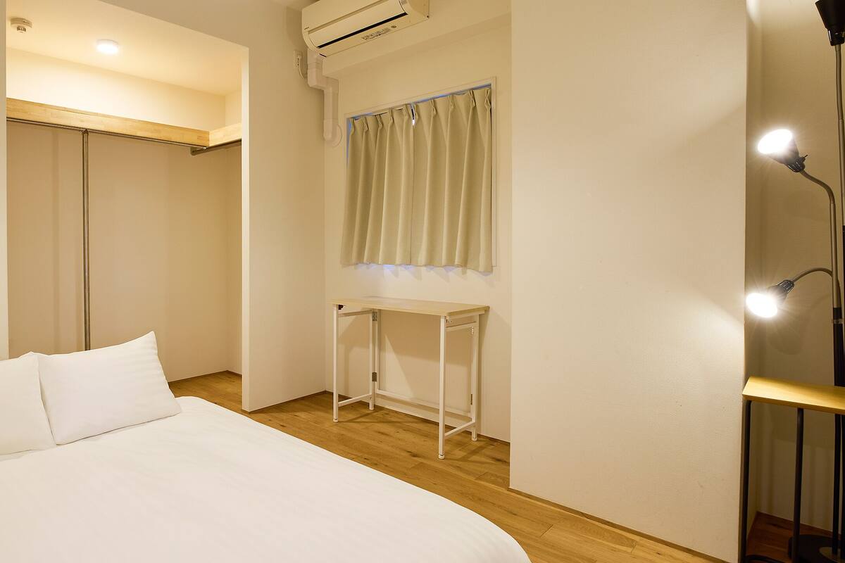 A bedroom with a bed, a desk, a wardrobe, and a window with curtains.