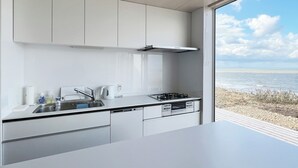 A modern kitchen with white cabinets, a stainless steel range hood, and a view of the sea through a large window.