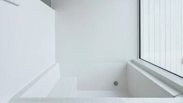 A white bathtub with a window, a white wall, and a small circular object on the floor.