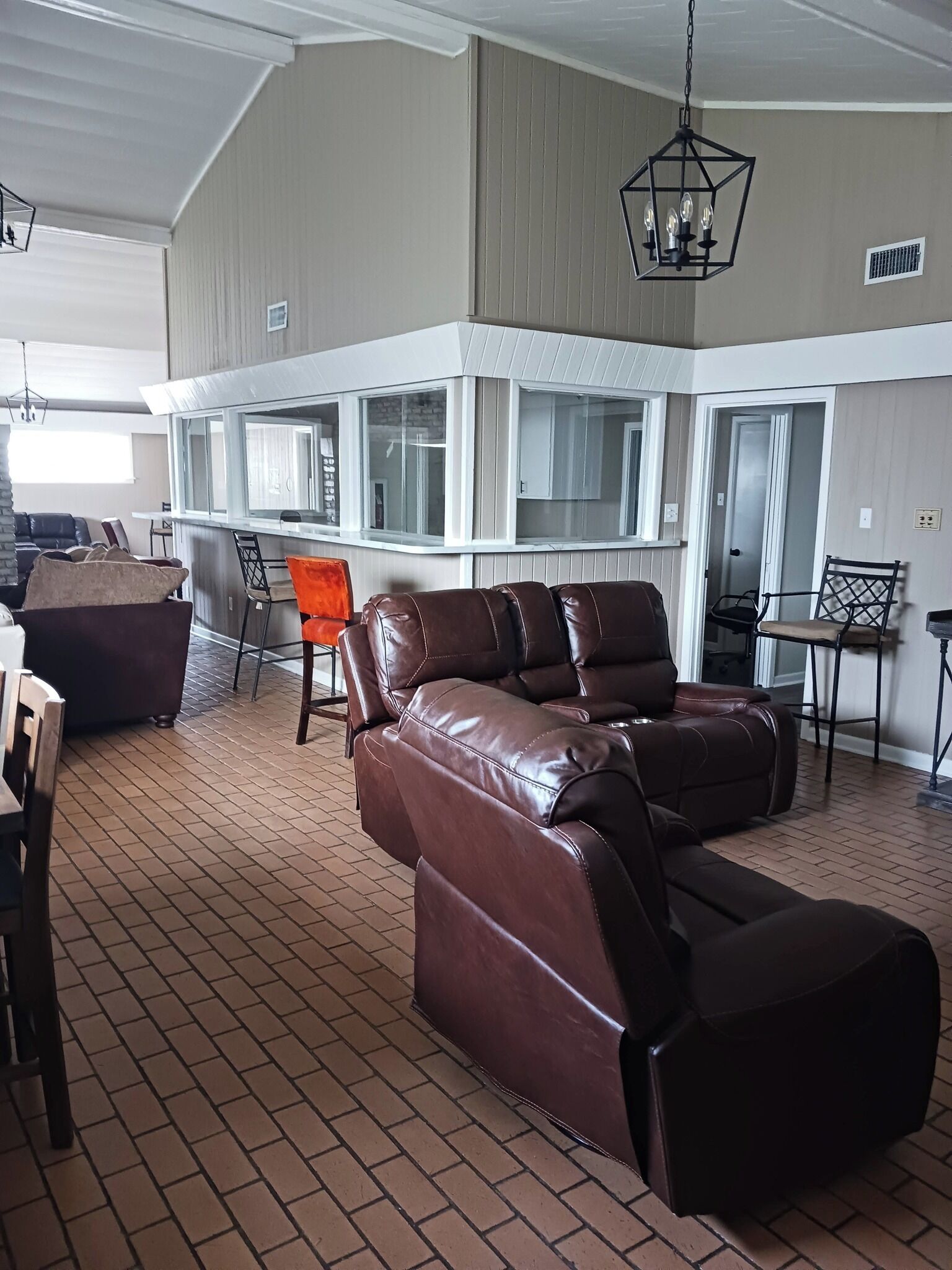 A spacious living area with a brown leather sofa, a dining table, and a kitchen area with large windows.