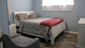 A bedroom with a bed, a nightstand, a chair, a window, and a dresser.