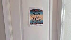 En hvid dør med et 'WELCOME'-skilt, en nøgle i låsen og et lille vindue for oven.