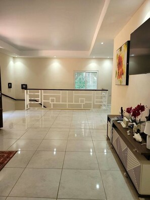 A spacious room with a tiled floor, a staircase with a railing, a large window, and a wall-mounted TV. - Casa Jungle Breeze – 4BR Stay Near West Bay (Roatán)