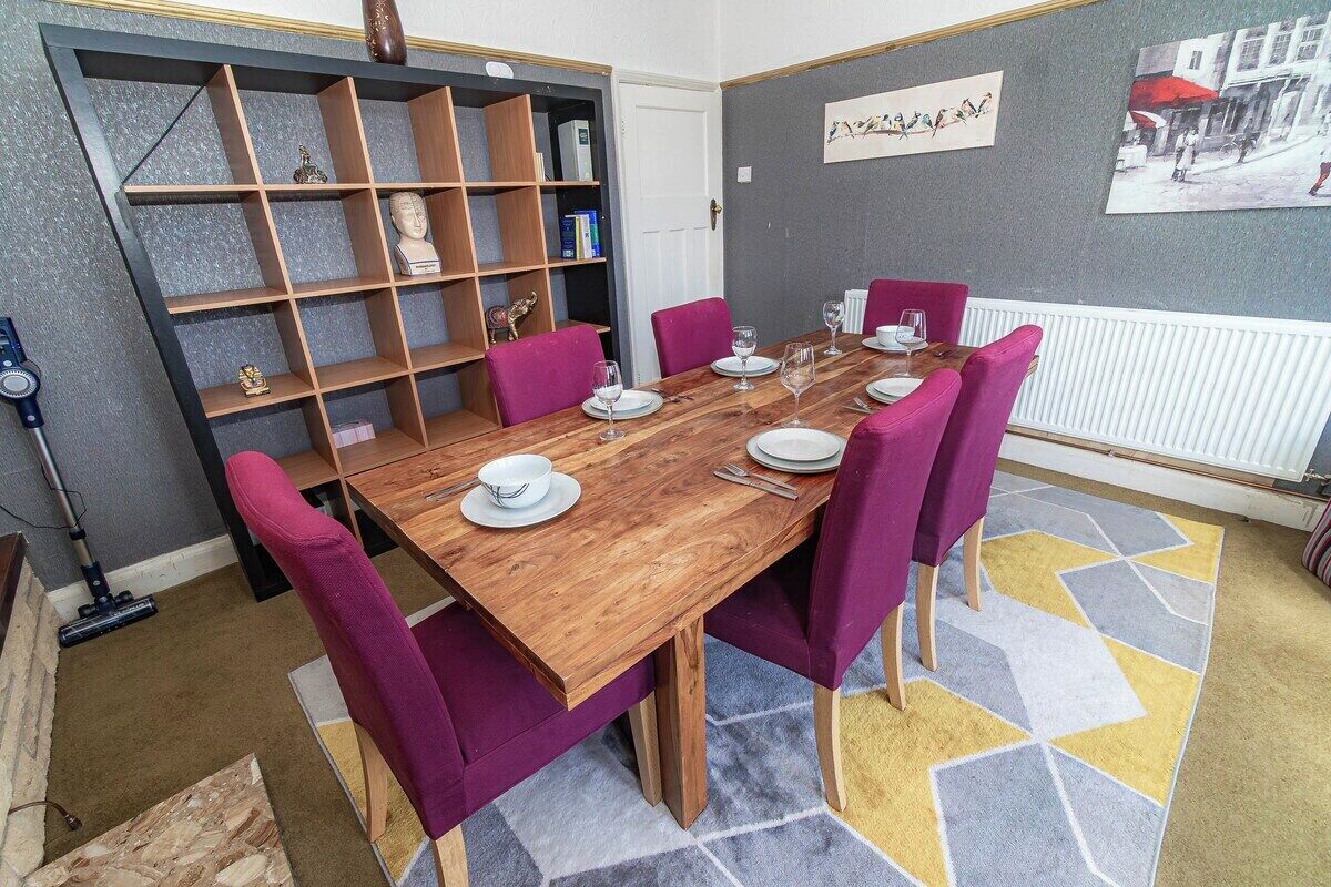 Une salle à manger avec une table en bois, des chaises violettes et une bibliothèque.