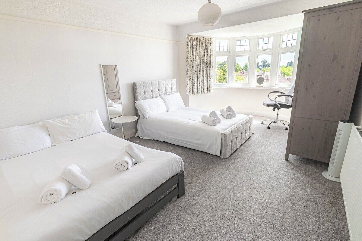 A hotel room with two beds, a desk, a chair, a wardrobe, and a window with curtains.