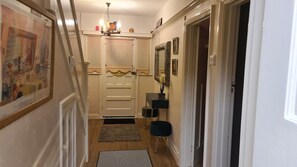 Un couloir avec une porte, une petite table sur laquelle se trouve un vase, et un miroir accroché au mur.