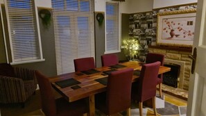 Un coin repas avec une table en bois et des chaises rouges, une cheminée et un mur orné de tableaux.