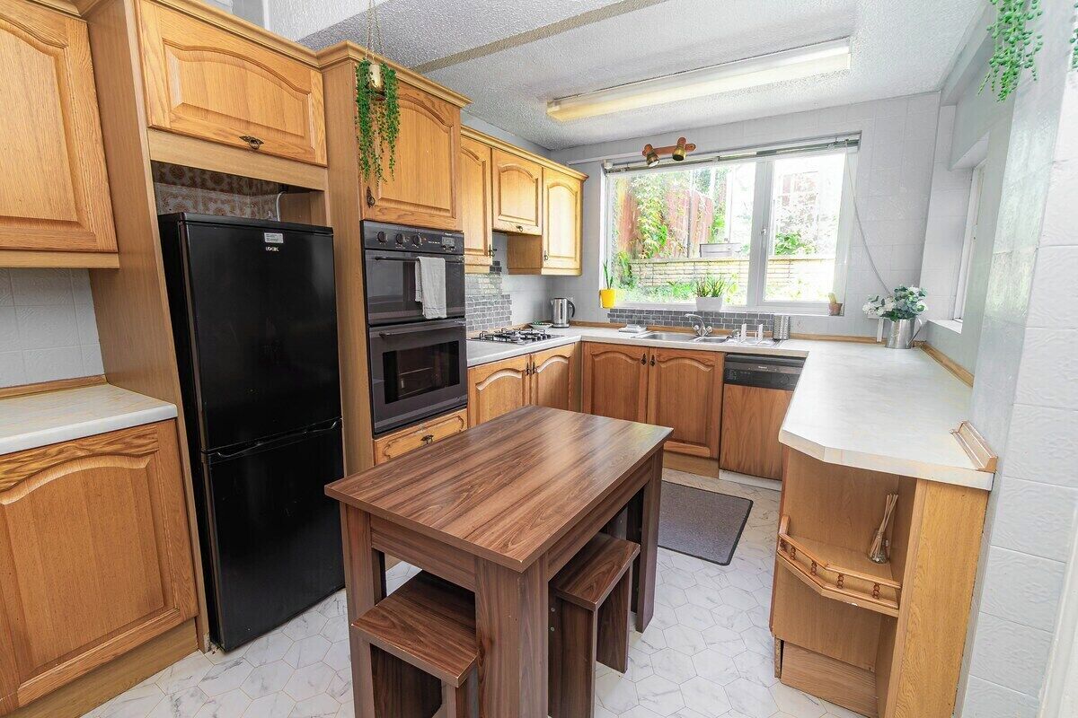 A kitchen with wooden cabinets, a black refrigerator, a stove, and a sink.